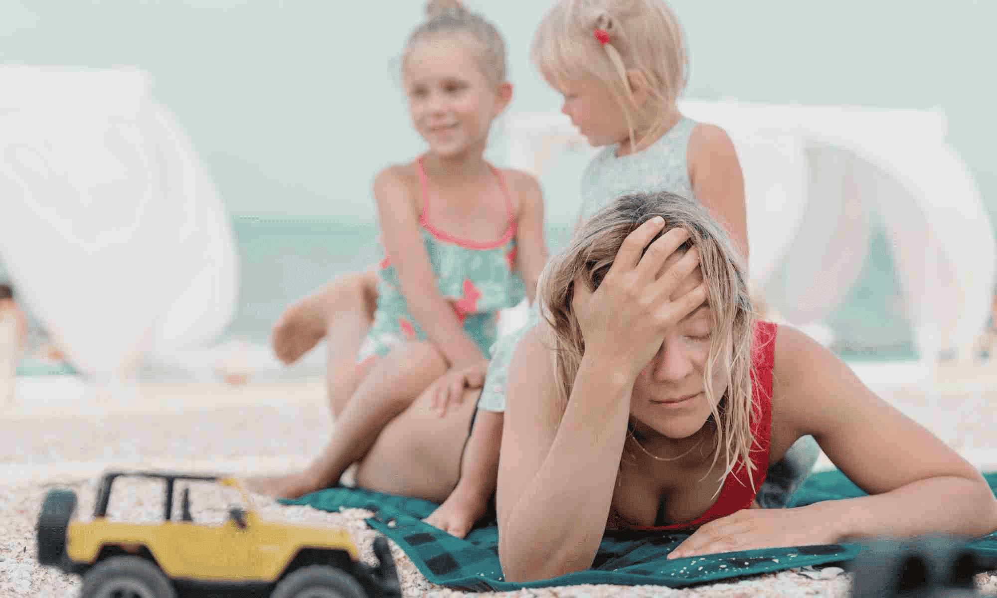 overwhelmed woman at beach with kids sitting on her